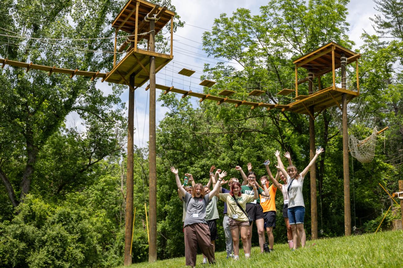 Participant in Cat Camp wave at the photo while standing under the ropes course
