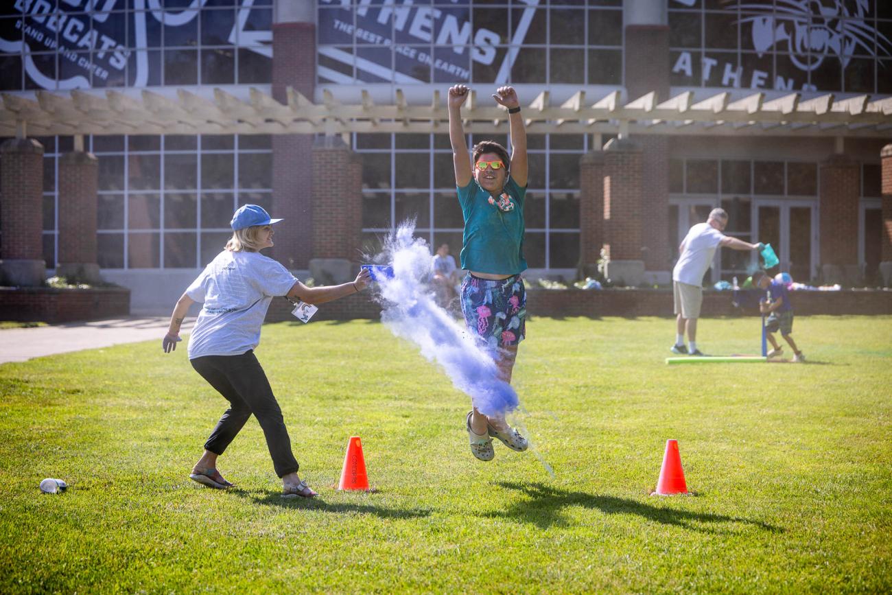 A camper jumps into the air to avoid colored smoke outside of the Ping Recreation Center during Cat Camp