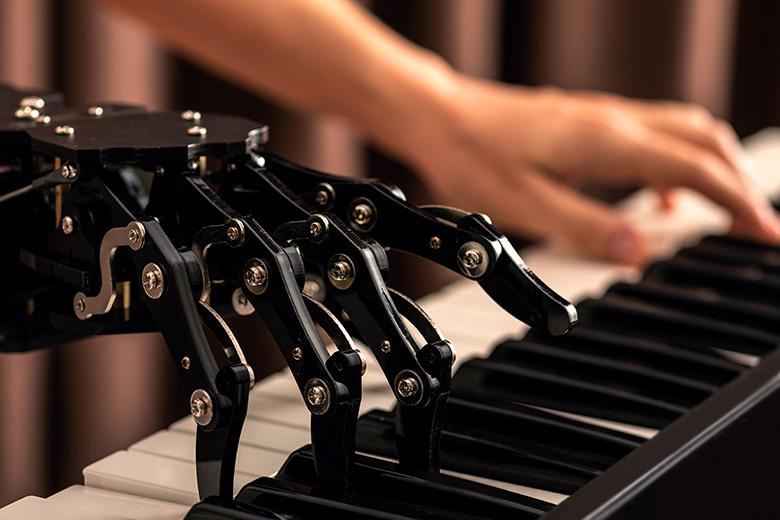 A robotic hand plays piano with a human hand.