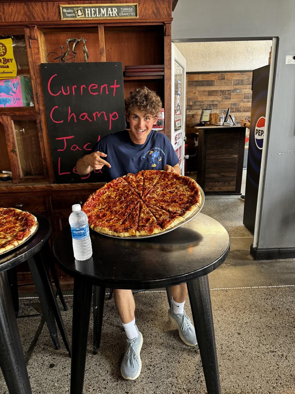 Jack Legath is shown with a very large pizza and a sign behind him that says "Current Champ Jack Legath"