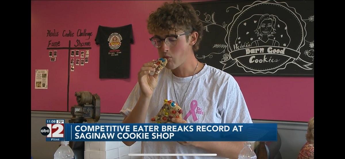 Jack Legath is shown eating a large cookie on a screenshot of a TV news program with the words on the screen saying "ABC-12 - Competitive eater breaks record at Saginaw Cookie shop"