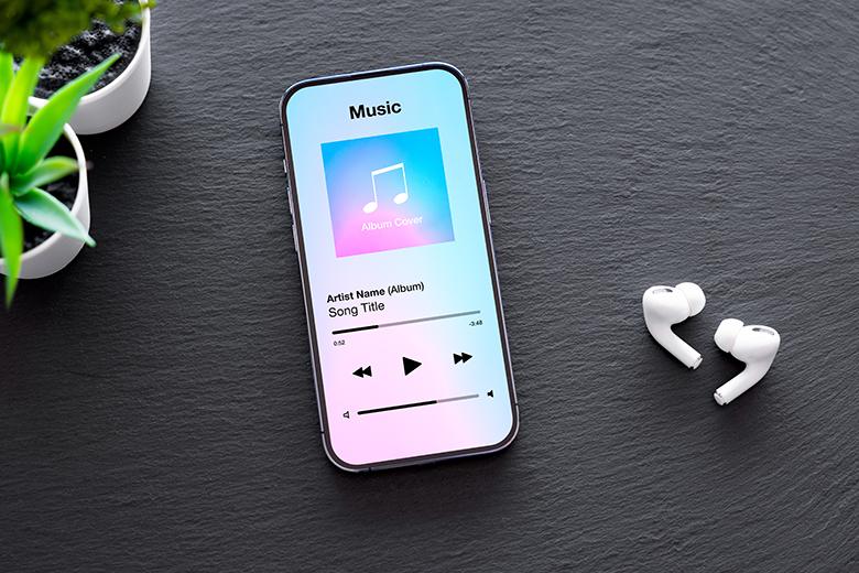 A phone with music playing sits next to a pair of wireless ear buds.