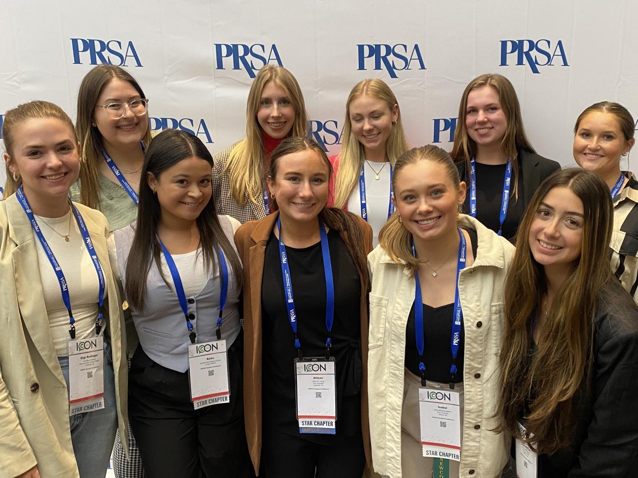 10 female college students wearing ICON conference lanyards pose in front of a PRSA backdrop