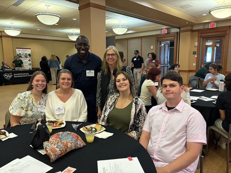 Students, faculty and staff are shown at a table at the welcome reception