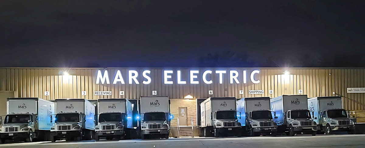 Trucks are parked next to the Mars Electric facility at night