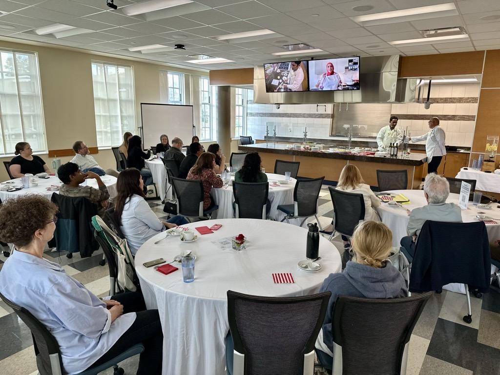 Yvonne Maffei presents the cooking demonstration on the video screen before a large crowd seated at tables