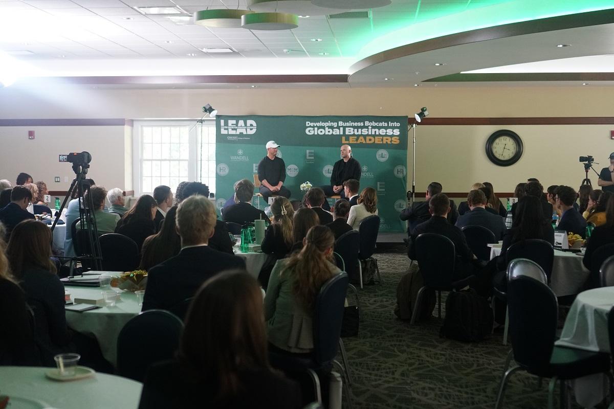 James Clear and Ryan Hawk speak in front of a large crowd in Nelson Commons