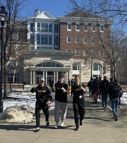 Three participants in the Leader Games Challenge walk on the sidewalk outside of Baker University Center while they take part in the challenge.
