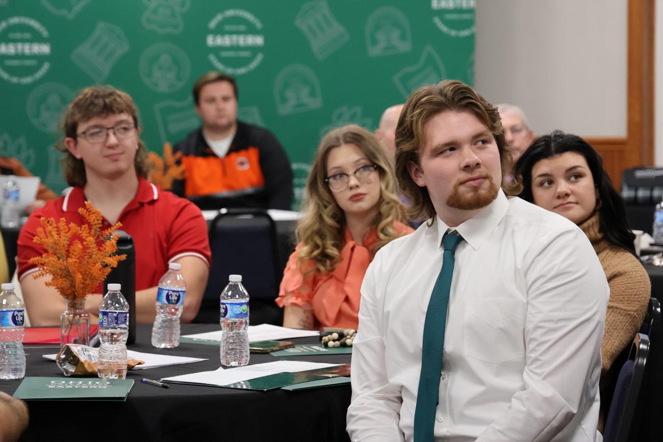 Group of students seated at round tables, looking intentionally towards a person not pictured