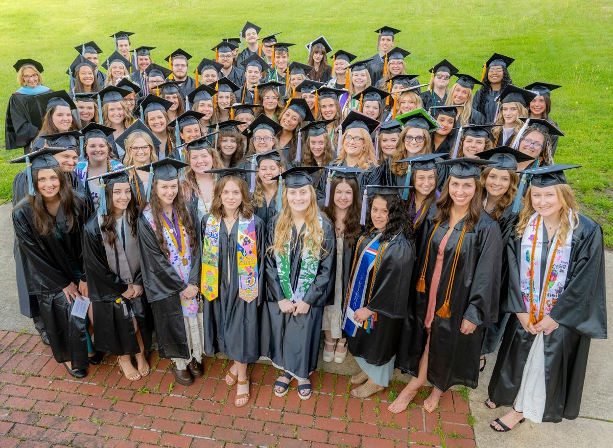 A large group of graduates wearing caps, gowns and cords stand together outside at Ohio University Lancaster at the Graduation Recognition Ceremony