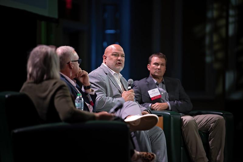 Four panel members sit on the stage and talk during a panel discussion event at the State of the Region Conference