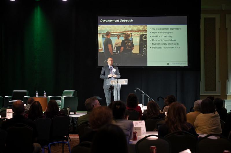 Joel Bradburne speaks on the stage with a graphic behind him that says "Development Outreach" during the conference.