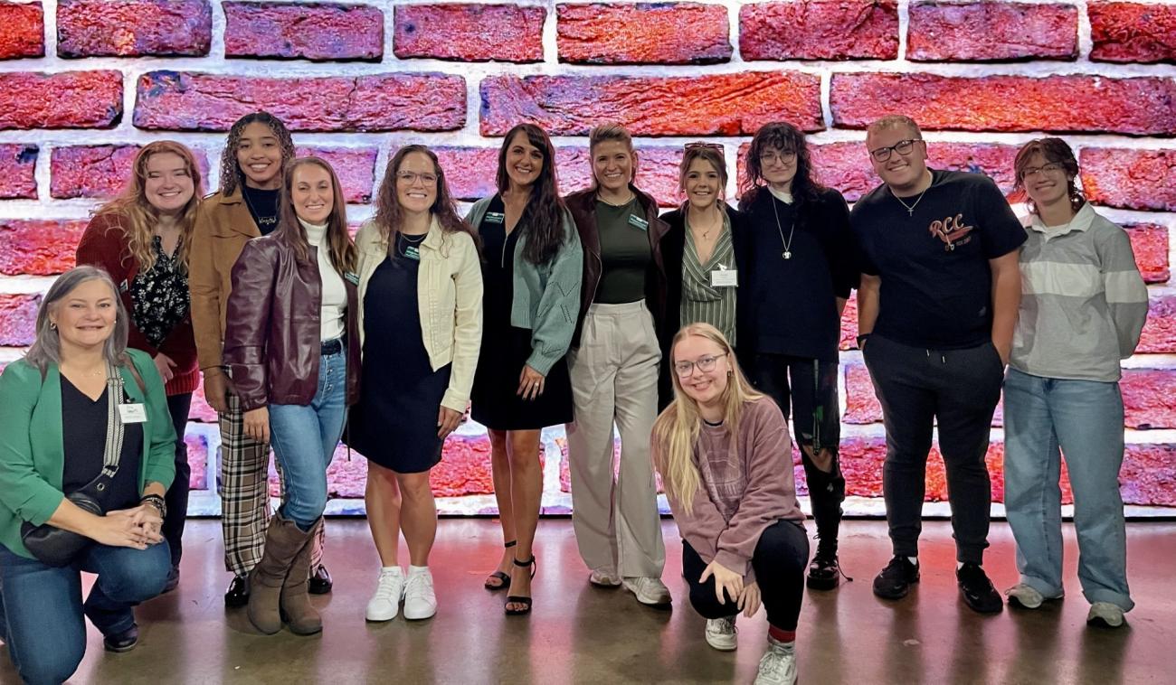 Scripps Young Alumni Council members stand together in front of a wall that is lit up to look like large bricks