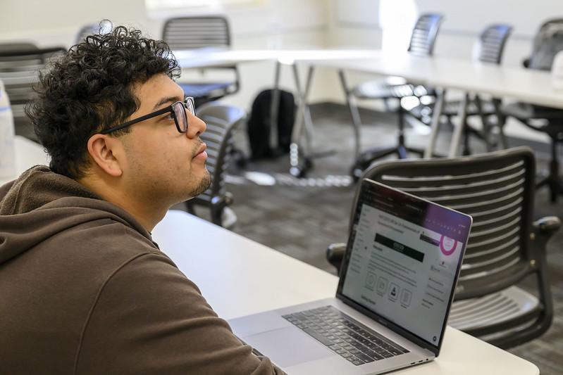 An OHIO student sitting next to a laptop computer listens to a presentation in class