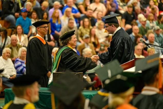 A graduate shakes hands with an OHIO leader in front of a large crowd at the Graduation Recognition Ceremony at OHIO Chillicothe