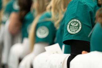 Close-up of arms in short-sleeved nursing uniforms bearing the HCOM mark at the 2023 White Coat Ceremony