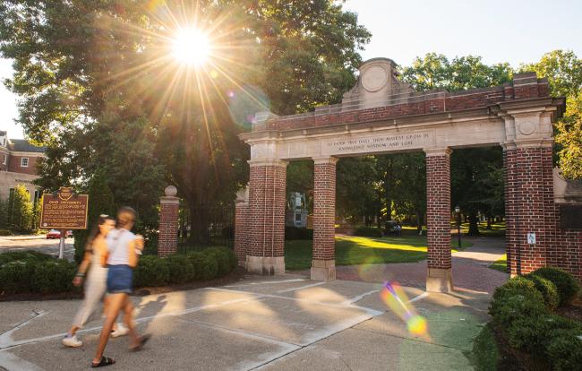 two people walk by the Alumni Gateway on a sunny morning