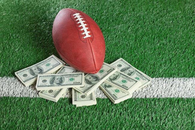 A football lays on a field next to a pile of money.