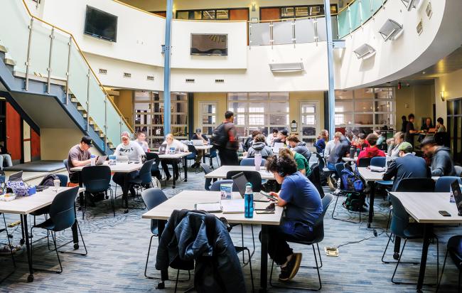 students sit at tables in a large, sunny atrium