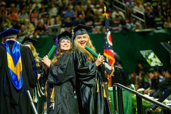 Two OHIO graduates in cap and gown celebrate after walking across the stage at Spring Commencement