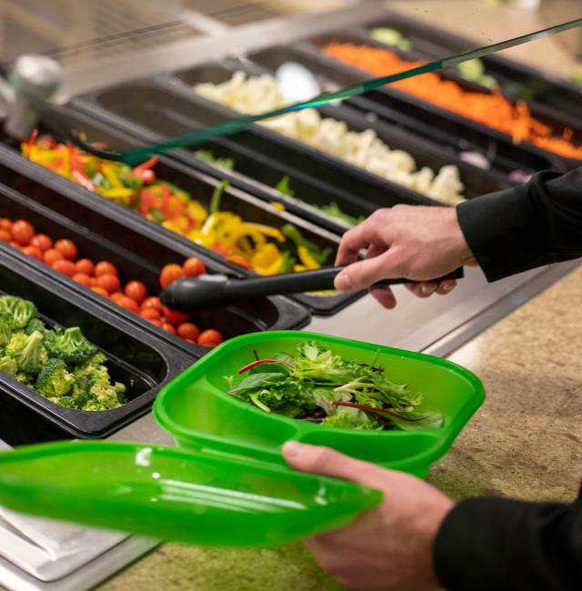 A student fills a to-go container with vegetables.