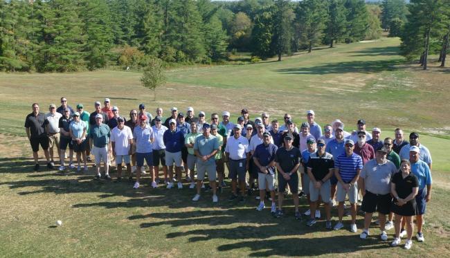 A large group of golfers stand together on the golf course at the Lonsbury Memorial Scholarship Golf Classic