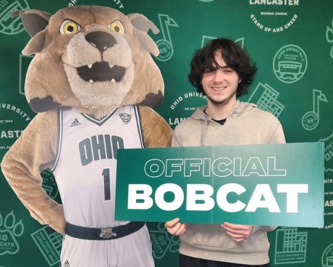 Peyton Wellman holds a sign that says 'Official Bobcat" while he stands next to a cardboard cutout image of Rufus