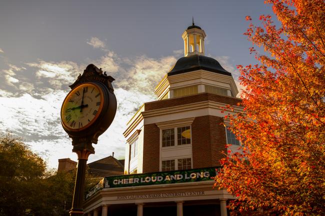 Baker University Center is shown next to the clock and colorful leaves during an evening in Fall