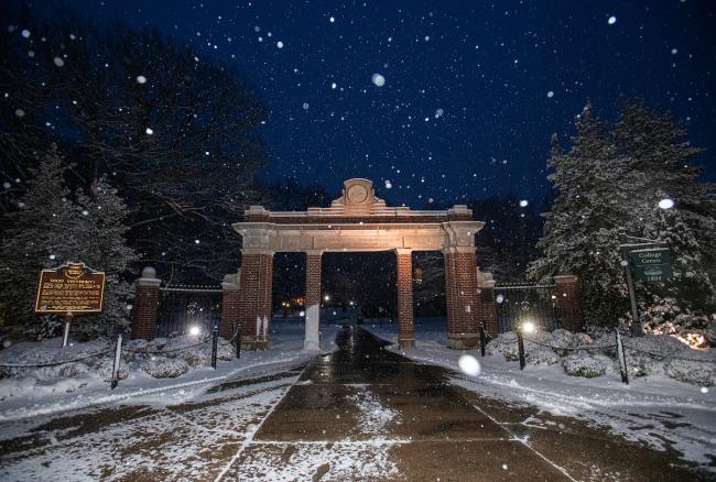 Snow falls on Alumni Gateway at night