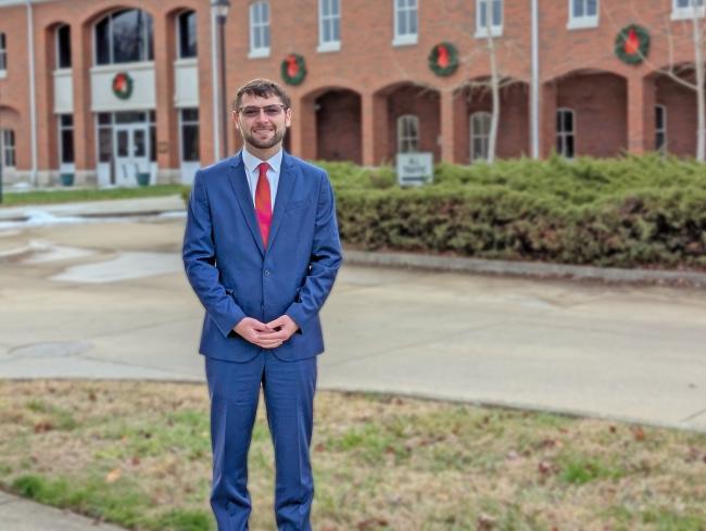 Man in suit stands in front of brick building