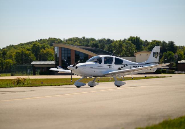 A plane with an OHIO logo on it is shown flying just above the aiport runway, and the Gordon K. Bush Airport is shown in the background