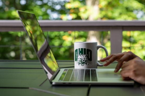  A photo of someone working on a laptop computer, and an OHIO coffee mug is next to the computer 