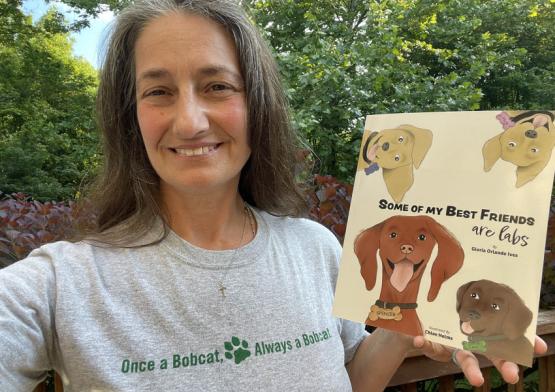  Gloria (Orlando) Ives, BSC ’88, shows off her Bobcat pride and her first book, which was designed by OHIO student-now-graduate CJ Herr, BFA ’22.