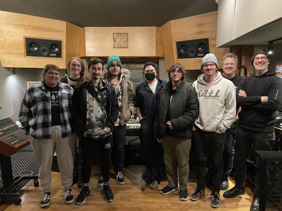  A group of students pose for a photo in a wood-paneled music studio 