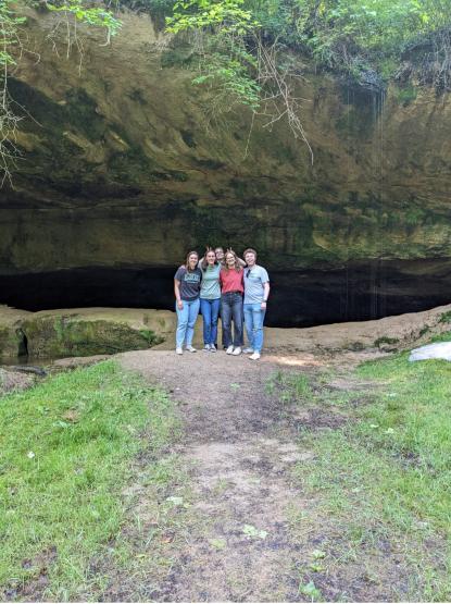 A group of students poses in front of a cave