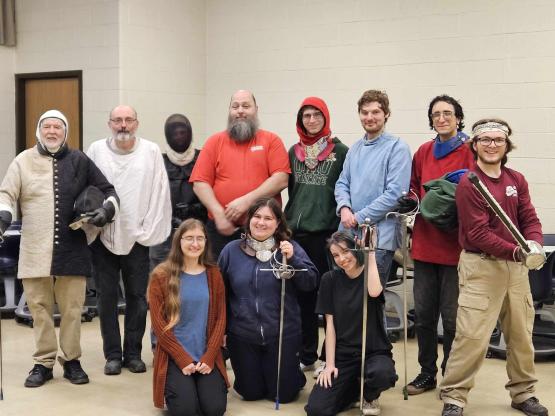 A group poses in Medieval clothing, wielding Medieval weapons and smiling