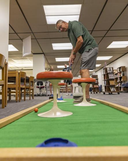 A man is shown playing putt-putt golf in Alden Library