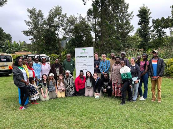  A group standing together in a forested area standing next to a sign that reads &amp;quot;Institue for Culture and Ecology.&amp;quot; 