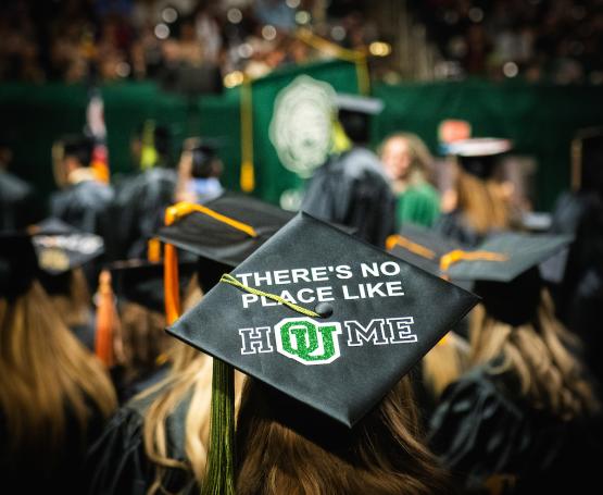 An OHIO student is shown wearing a graduation cap that says "There's No Place Like HOUme at Fall Commencement 2023