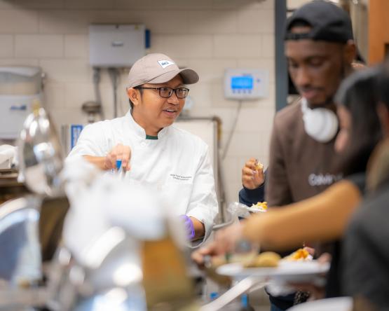  A chef is pictured at a banquet with other people serving themselves in the foreground 