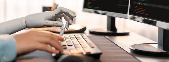  A robot hand typing on computer keyboard next to a human hand. 