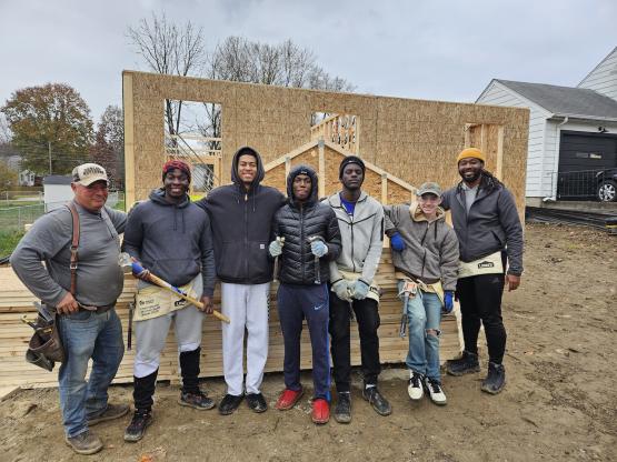  A group of men stands in front of a house mid-construction 