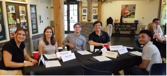  A group of students are seated at a conference table, smiling at the camera 