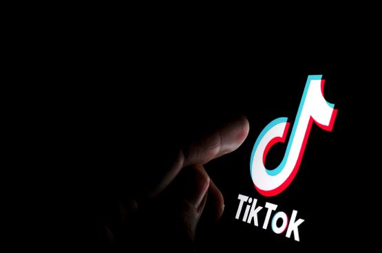  A person&amp;#039;s finger points to a digitally lit TikTok logo on a dark background 