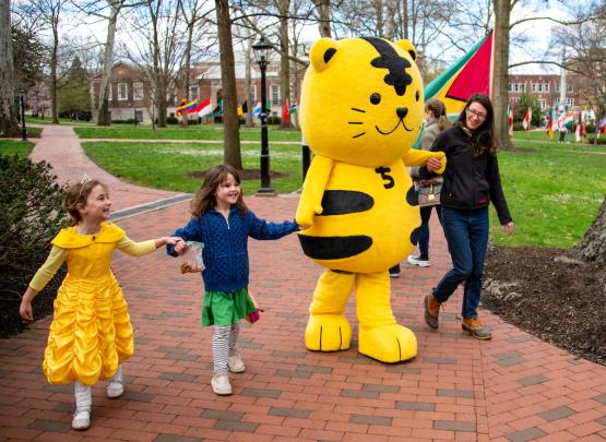 The Chubu University mascot is shown with children and an adult on the College Green during the International Street Fair