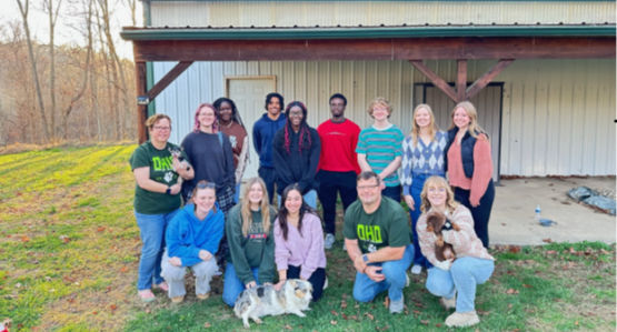 A Learning Community class poses for a photo while outside, and two pets are also in the image