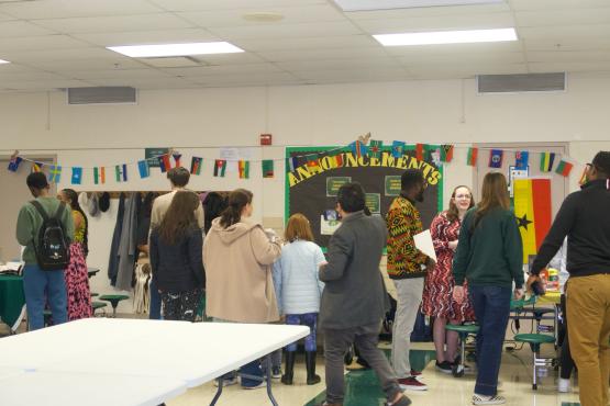 A group of people inside a school surrounding tables.