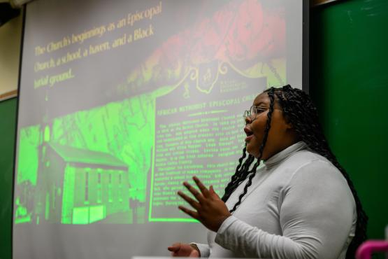 A student presents in front of a screen showing historical research