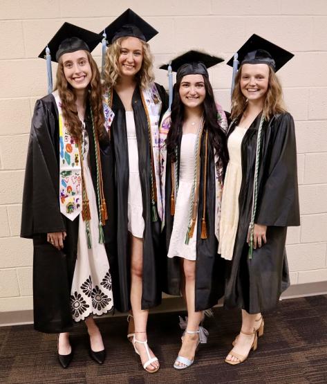 Four OHIO Lancaster Graduates wearing graduation caps and gowns stand together for a photo