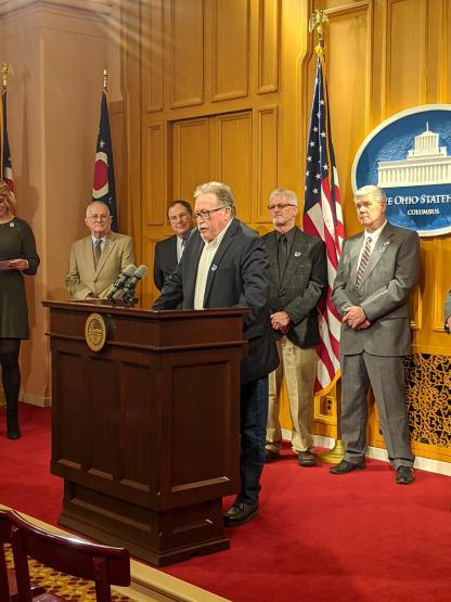 Greg Fraunfelter is shown speaking in front of other Ohio leaders at the Ohio Statehouse